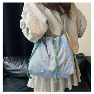 Detail of blue denim bucket bag featuring yellow flower embroidery and green drawstrings