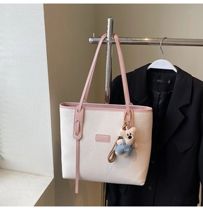 Detail of a large beige tote bag with pink straps and a cute plush bear charm