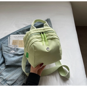 Detail of light green mini backpack featuring dual zippers and metal logo on nylon fabric