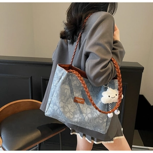 Close-up of blue floral tote bag with brown woven handle and leather logo tag details