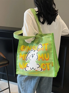 Green canvas tote bag with cartoon rabbit print worn by model for casual street style