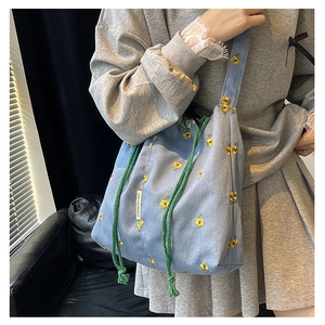 Detail of light blue bucket bag with yellow flower embroidery and green drawstring