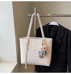 Detail of cream tote bag with pebble leather texture and cute bear charm pendant