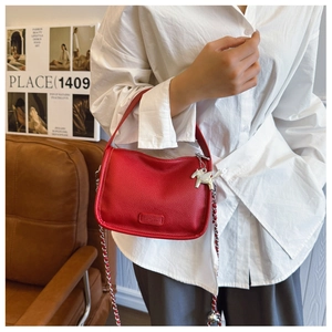 Detail of red lychee textured leather crossbody bag with silver horse pendant charm