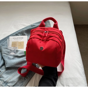 Detail of red nylon multi-layer crossbody bag with metal M logo and strap on bed