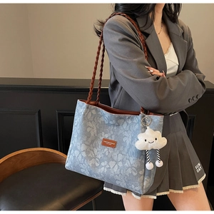 Close-up of blue floral tote bag with brown woven handle and cute cloud plush charm