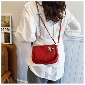 Detail of red pebbled leather crossbody bag with silver chain strap and horse pendant