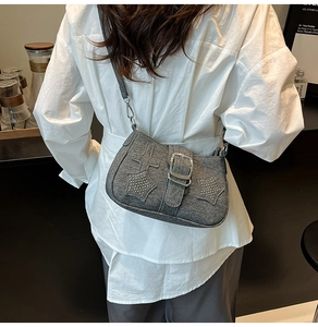 Gray denim crossbody bag featuring star rivets and metallic buckle in a cafe setting