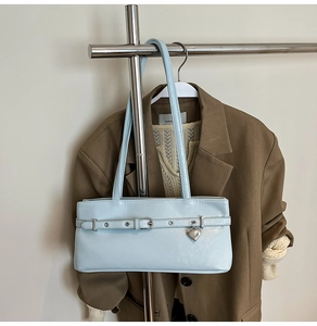 Detail of light blue patent leather underarm bag with silver heart charm and metal eyelets