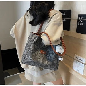 Detail of grey floral tote bag with brown woven strap and white cloud charm accessory