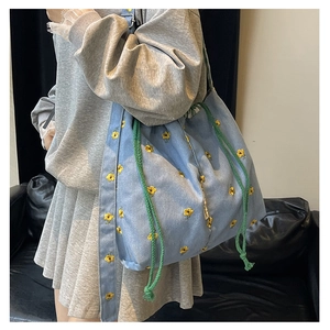 Detail of light blue denim bucket bag with yellow flower embroidery and green drawstring