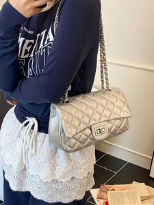 Silver quilted crossbody bag with metal chain strap worn by a model in a minimalist setting