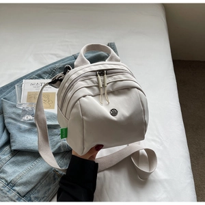 Close-up of cream canvas shell bag with dual zippers and M Fashion logo detail