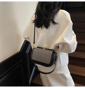 Detail view of a two-tone leather crossbody bag worn by a model on a wooden staircase