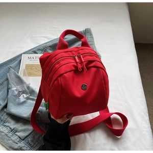 Detail of red nylon mini backpack showing dual zip pockets and round metal logo