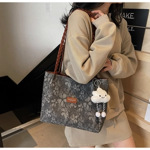 Detail of grey floral tote bag with brown woven handles and cloud charm shown on shoulder
