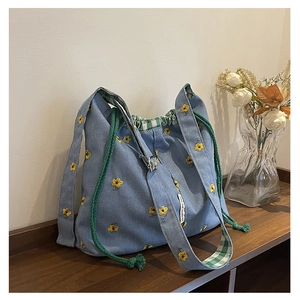 Detail of light blue bucket bag with yellow flower embroidery and green plaid lining