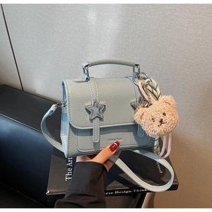 Gros plan d'un sac à main en cuir bleu clair avec fermoir étoile et breloque ours