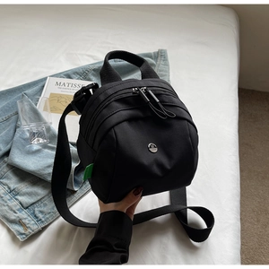 Detail shot of mini black canvas backpack featuring a circular metal M logo on bed