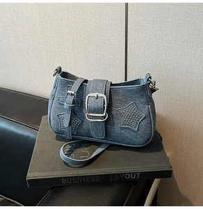 Close-up of blue denim shoulder bag featuring silver rivet stars and metallic buckle