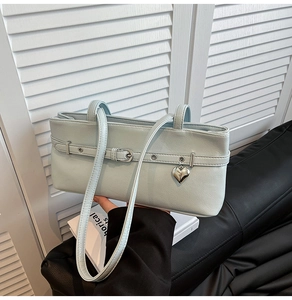 Detail of light blue leather underarm bag featuring a metallic heart pendant and buckle strap