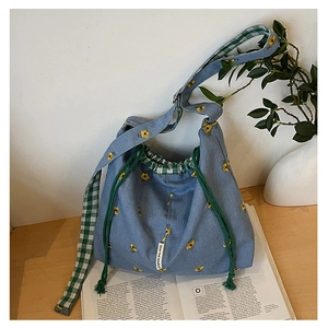 Detail of blue canvas bucket bag featuring floral embroidery and plaid drawstring closure