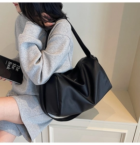 Side view of large black pebble leather hobo bag worn by model on minimalist white stairs