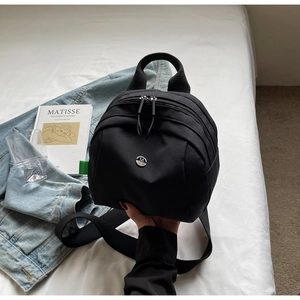 Fashionable black nylon mini backpack featuring a round metallic M logo and zip closure