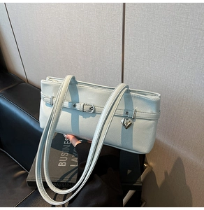 Detail of light blue leather shoulder bag with decorative buckle straps and heart pendant