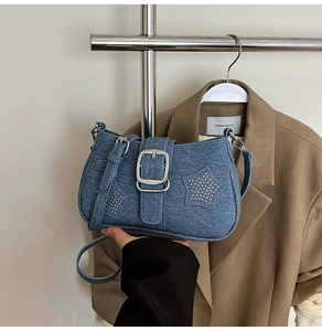 Detail of blue denim shoulder bag featuring silver buckle and star-shaped metal rivets