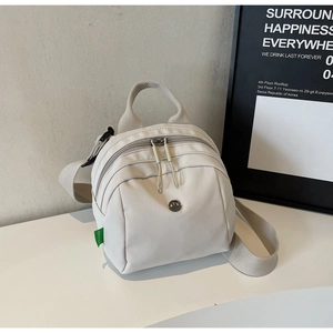 Detail view of cream nylon backpack featuring brand tag and adjustable webbing strap