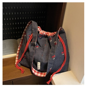 Close-up of denim tote bag with cherry embroidery, drawstring top and plaid lining