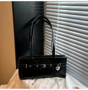 Detail of a black glossy shoulder bag with silver eyelets and a heart charm on white fabric
