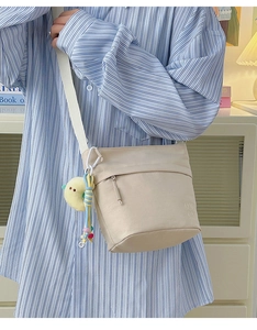 Dettaglio borsa a secchiello in nylon beige con tracolla larga e ciondolo a forma di papera