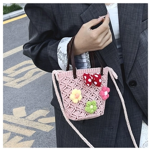 Detail of pink hand-woven beach bucket bag with floral accents on a grey blazer outfit