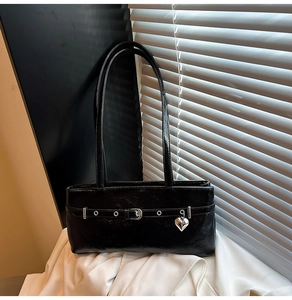 Close-up of black glossy underarm bag with belt buckle detail and silver heart pendant