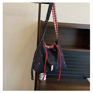 Detail of navy denim bucket bag featuring red cherry embroidery and a checkered strap