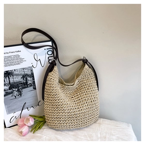 Détail du sac seau en paille tressée beige avec bandoulière en cuir brun et boucle métal