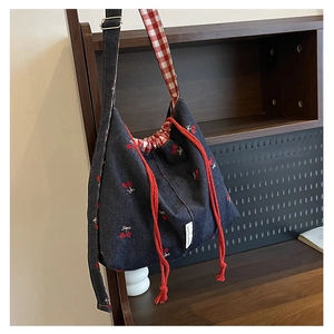 Detail of denim bucket bag featuring cherry embroidery and red checkered lining