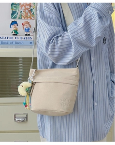 Dettaglio borsa a tracolla in tela beige con ricamo OMQ CNH e ciondolo a luna