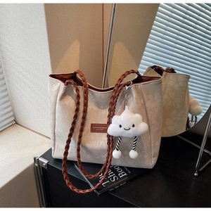 Detail of beige tote bag with woven straps, brown leather patch, and cloud charm decoration