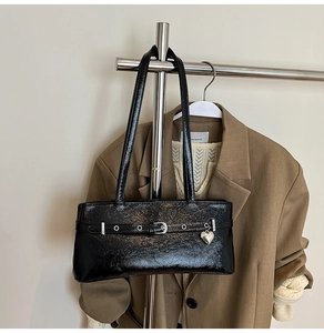 Detail of black glossy underarm bag featuring silver eyelets and a heart-shaped charm