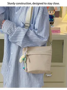 Dettaglio della borsa a secchiello in nylon beige con lettere ricamate e ciondolo peluche
