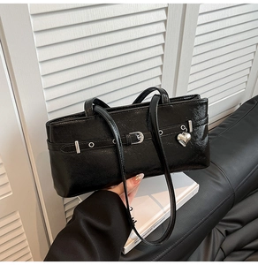Macro shot of black patent leather shoulder bag with silver heart charm and metal buckle