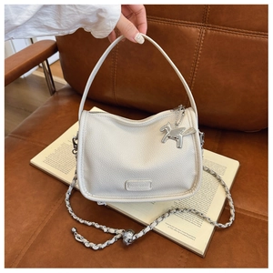 Close-up of ivory lychee leather handbag with silver chain strap and horse charm detail