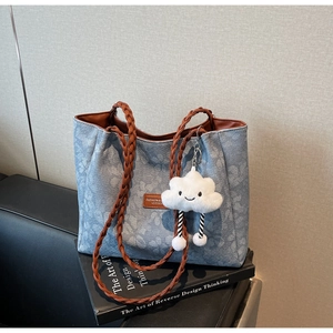 Detailed shot of blue denim tote bag with white floral pattern and woven leather handles