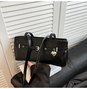 Detail of black patent leather shoulder bag with silver buckle strap and heart pendant