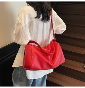 Close-up of bright red litchi grain leather shoulder bag with wide strap and metal buckle