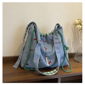 Detail of blue denim bucket bag featuring red cherry embroidery and green checkered drawstring