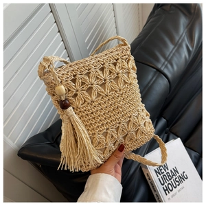 Détail du motif floral au crochet sur le sac de téléphone en paille beige à glands